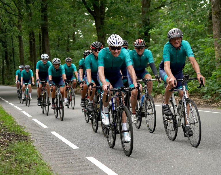 Een groep wielrenners van Cyclo'78 in groen/blauwe tenue rijden in een sliert over een asfaltweg