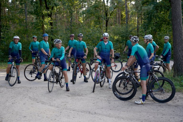 Een groep fietsers staat stil op een kruising op een zandpad in een bos